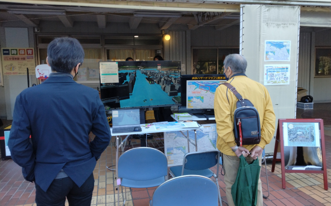 写真：地域イベントで浸水シミュレーションの映像を見る男性2名